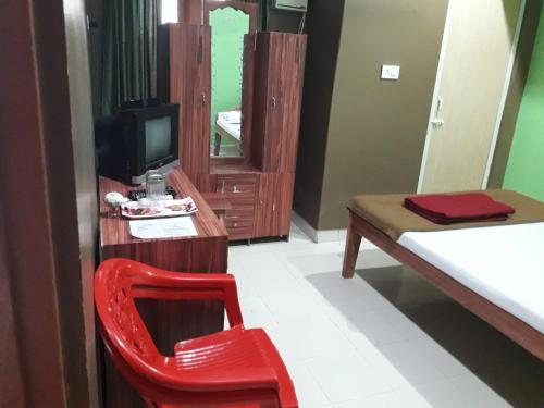 a red chair in a room with a bed and a television at Roxel Inn in Port Blair