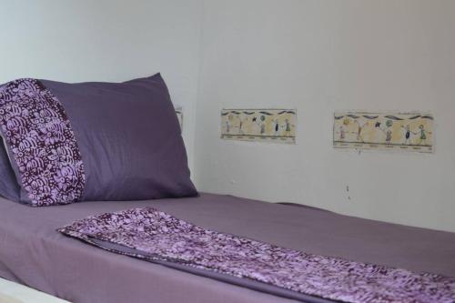 a bed with a purple blanket and two pictures on the wall at Dragonfly Cottage in Bagamoyo
