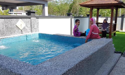 a group of children sitting next to a swimming pool at Jauzara Homestay Berkolam Renang in Port Dickson