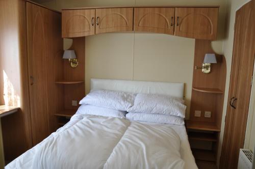 a bedroom with a bed with white sheets and wooden cabinets at Caravan 6 Berth North Shore Holiday Centre with 5G Wifi in Winthorpe