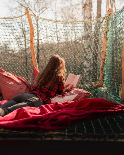 a woman laying on a hammock reading a book at Les Cabanes De Pyrene in Cazarilh