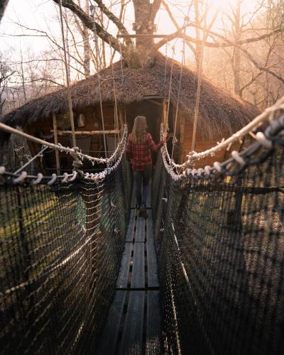 a woman walking across a suspension bridge in a forest at Les Cabanes De Pyrene in Cazarilh