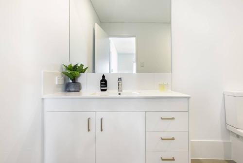 Baño blanco con lavabo y espejo en Minimalist Penthouse Condo with Skyline Vistas en Perth