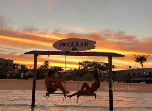a man and woman sitting on chairs under an umbrella on the beach at Sandy Heaven Maldives in Gulhi