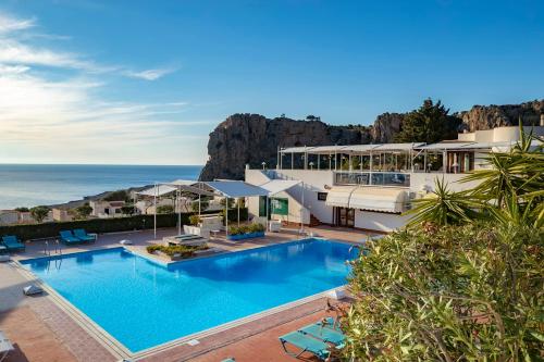 a resort with a large swimming pool next to the ocean at Hotel Pocho in San Vito lo Capo
