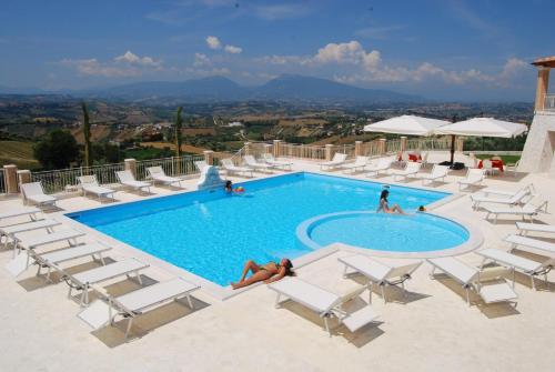 una piscina con sillas blancas y un grupo de personas en Incantea Resort, en Tortoreto Lido