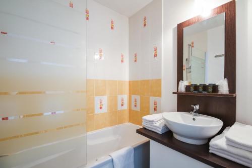 a bathroom with a sink and a tub and a mirror at Vacancéole - Les Jardins de l'Amirauté in Les Sables-d'Olonne