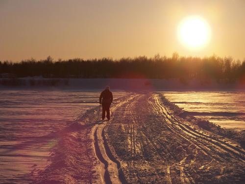 a man walking down a snow covered road with the sun in the background at E-City B&B in Tornio