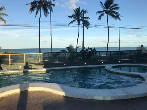 uma piscina com palmeiras e o oceano ao fundo em Flat no Hotel Ritz Suites em Maceió