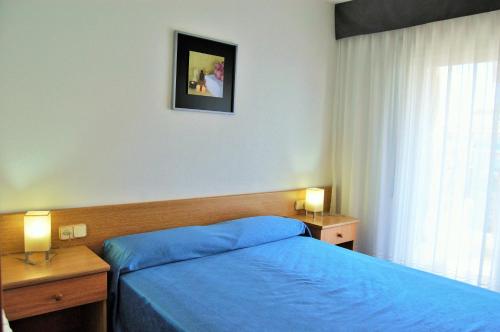 1 dormitorio con 1 cama azul, 2 mesas y una ventana en Apartamento Sun Garden Lloret de Mar, en Lloret de Mar