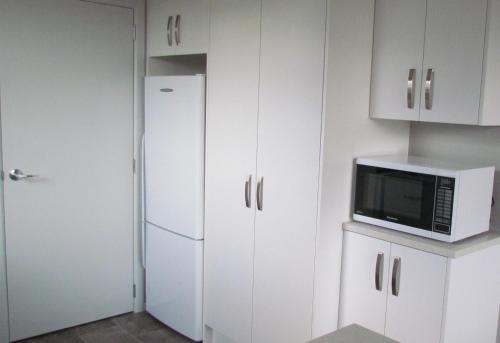 eine Küche mit weißen Schränken, einer Mikrowelle und einem Kühlschrank in der Unterkunft Birchwood Cottages in Te Anau