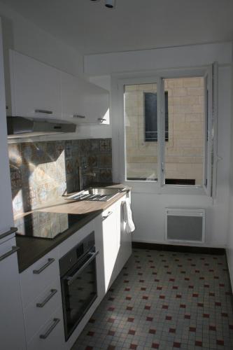 une cuisine avec des armoires blanches, un évier et une fenêtre dans l'établissement LE HARAS, à Libourne