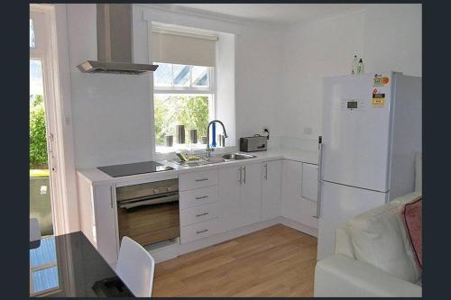 a white kitchen with a refrigerator and a sink at Hobart Colonial Apartment in Hobart