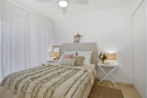 a white bedroom with a bed and a table with lamps at 23 At The Islander in Point Lookout