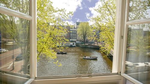 a window with a view of a river with boats in it at Hotel Nes Amsterdam in Amsterdam