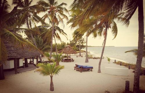 a beach with tables and palm trees and the ocean at Kilwa Beach Lodge in Kilwa Masoko
