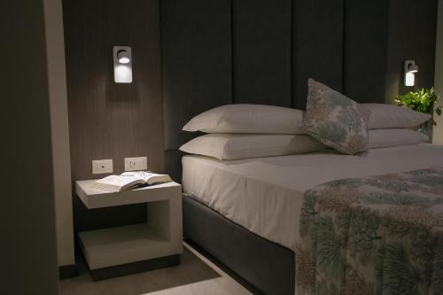 a bedroom with a bed and a side table with a book at Mosella Suite Hotel in Sottomarina