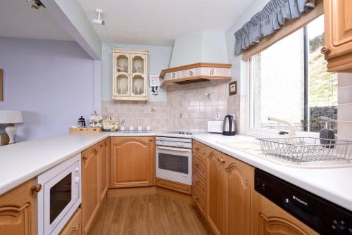 eine Küche mit Holzschränken, einem Waschbecken und einem Fenster in der Unterkunft Tweed Cottage in Jedburgh