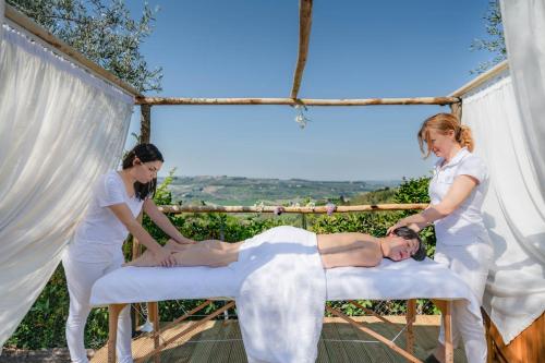 Dos mujeres están ayudando a un hombre acostado en una cama en Villa I Barronci Resort & Spa, en San Casciano in Val di Pesa