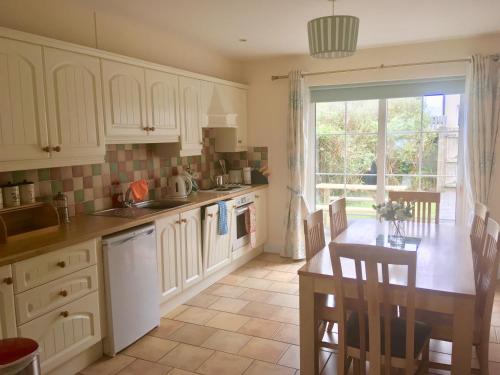 cocina con armarios blancos, mesa y ventana en Fuchsia House en Valentia Island