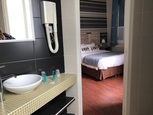 a bathroom with a sink and a bed in a room at Hôtel d'Arromanches Pappagall in Arromanches-les-Bains