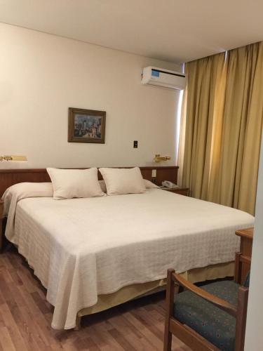 a bedroom with a large white bed and a chair at Hotel Cervantes in Mendoza