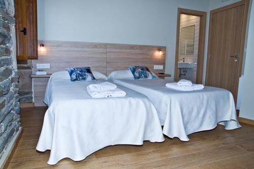 two beds in a room with white sheets and towels at PENSION SERRANO in Sarria