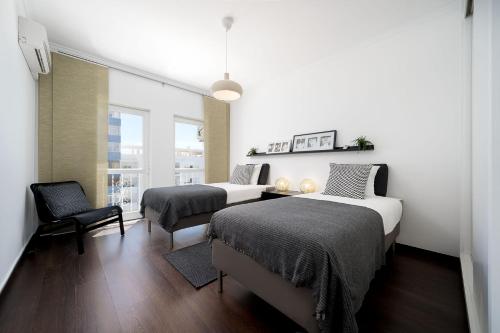 a bedroom with two beds and a chair and a window at Beautiful Modern Apartment in Olhão, Algarve in Olhão