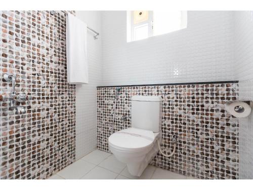 a bathroom with a toilet and a tile wall at Olive Serviced Apartments HSR Layout in Bangalore