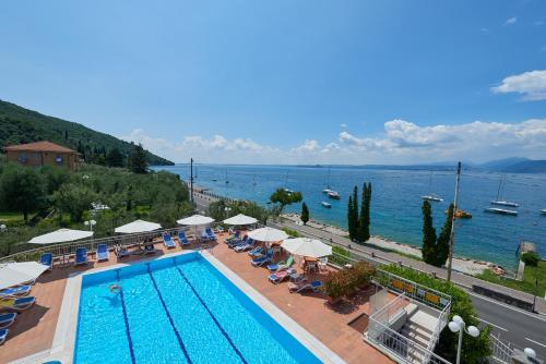 a swimming pool with chairs and umbrellas next to the ocean at Hotel Benacus Torri del Benaco in Torri del Benaco