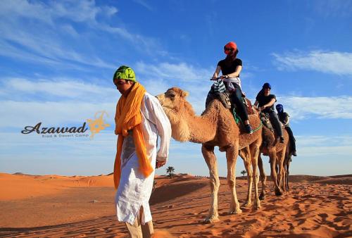 Eine Gruppe von Menschen, die auf Kamelen in der Wüste reiten in der Unterkunft Azawad Luxury Desert Camp in Merzouga