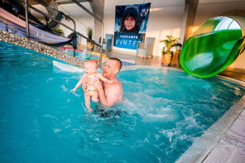 a man holding a baby in a swimming pool at Hvide Sande Beach Apartments in Hvide Sande