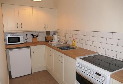 een keuken met witte kasten, een wastafel en een magnetron bij 2 Bell Street in Talgarth