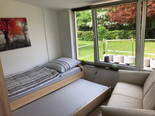 Bett in einem Zimmer mit Sofa und Fenster in der Unterkunft Ruhiges Apartment mit Blick in den Garten in Alsdorf