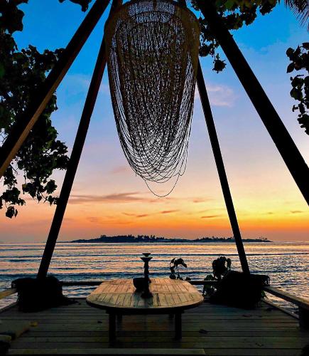 a hammock and a table on a dock with a sunset at Samura Maldives Guest House Thulusdhoo in Thulusdhoo