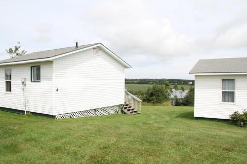 a white house with a yard next to a building at Chalets Grand Pre Cottages in North Rustico