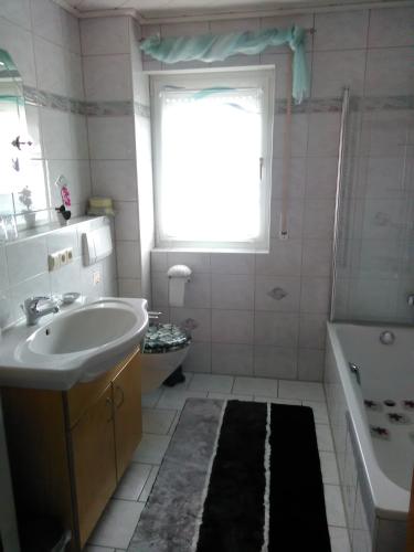 ein Bad mit einem Waschbecken, einer Badewanne und einem Fenster in der Unterkunft Ferienwohnung Hops in Daisendorf