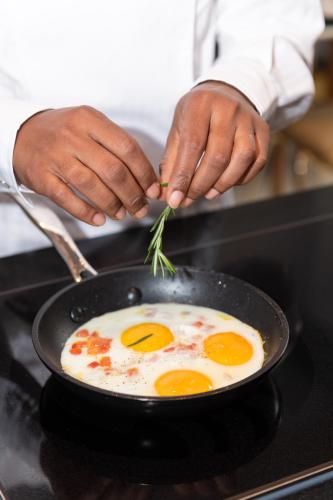 a person cooking eggs in a pan on a stove at Boutique Hotel Sablon by CW Hotel Collection in Bruges