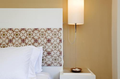 a bed with a white comforter next to a lamp at Relais Parco Cavalonga in Donnafugata