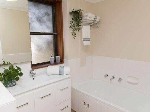 Un baño con bañera, lavabo y ventana. en Taranaki Beach House, en Port Macquarie