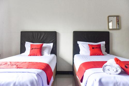 two beds with red pillows in a room at RedDoorz near Sultan Hasanuddin Airport 2 Makassar in Makassar