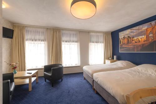 een hotelkamer met 2 bedden en een bureau met een stoel bij De Waag in Makkum