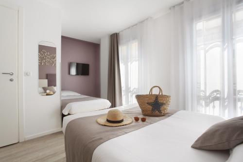 ニースにあるHôtel Alcôve Niceのベッド2台、ベッドの上に帽子が備わるホテルルームです。