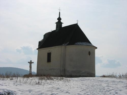 a church with a cross on a snow covered field at Penzion Chalupka in Spišské Podhradie