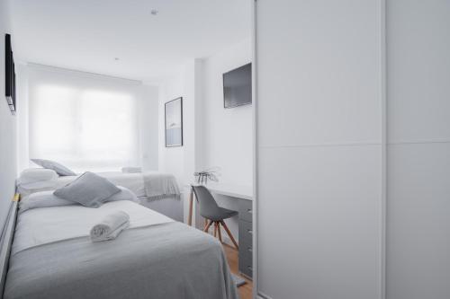 a white bedroom with two beds and a chair at GOXUE HOME in Donostia-San Sebastián