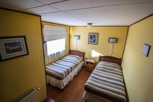 a small room with two beds and a window at Hostal Alcázar in Puerto Natales