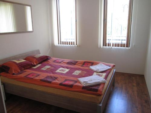 a bedroom with a bed with a quilt and two windows at MD Alexander Services Apartments in Bansko