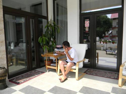 a man sitting at a table talking on a cell phone at Pensiunea Eden in Băile Olăneşti