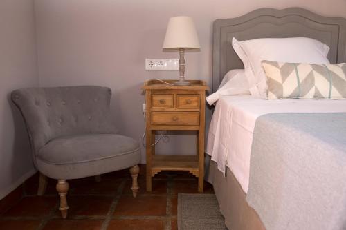 a bedroom with a bed and a chair and a lamp at Hotel Rural Las Tejuelas in Valdecaballeros