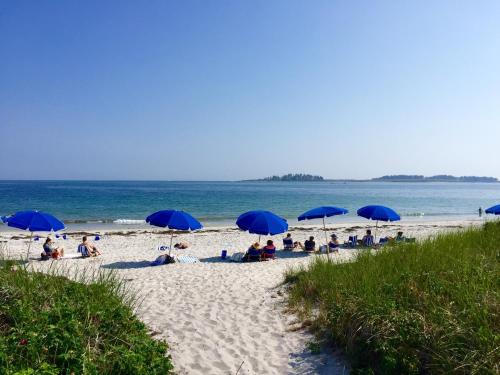 a group of people sitting under blue umbrellas on a beach at Inn By the Sea in Cape Elizabeth
